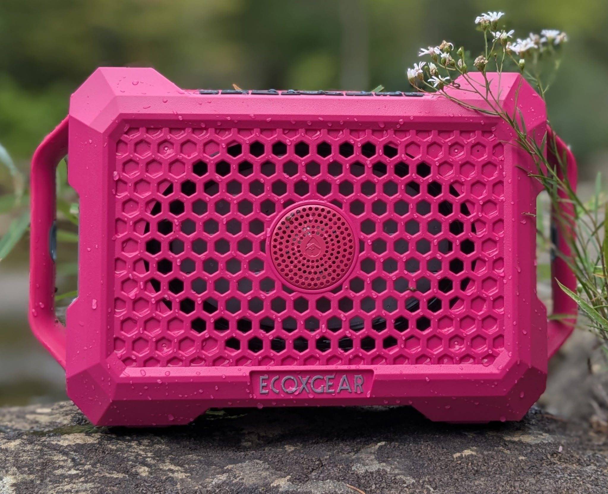 Pink EcoXGear Defender speaker on a natural background with water droplets